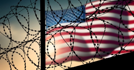 American flag with a barbed wire fence in the foreground